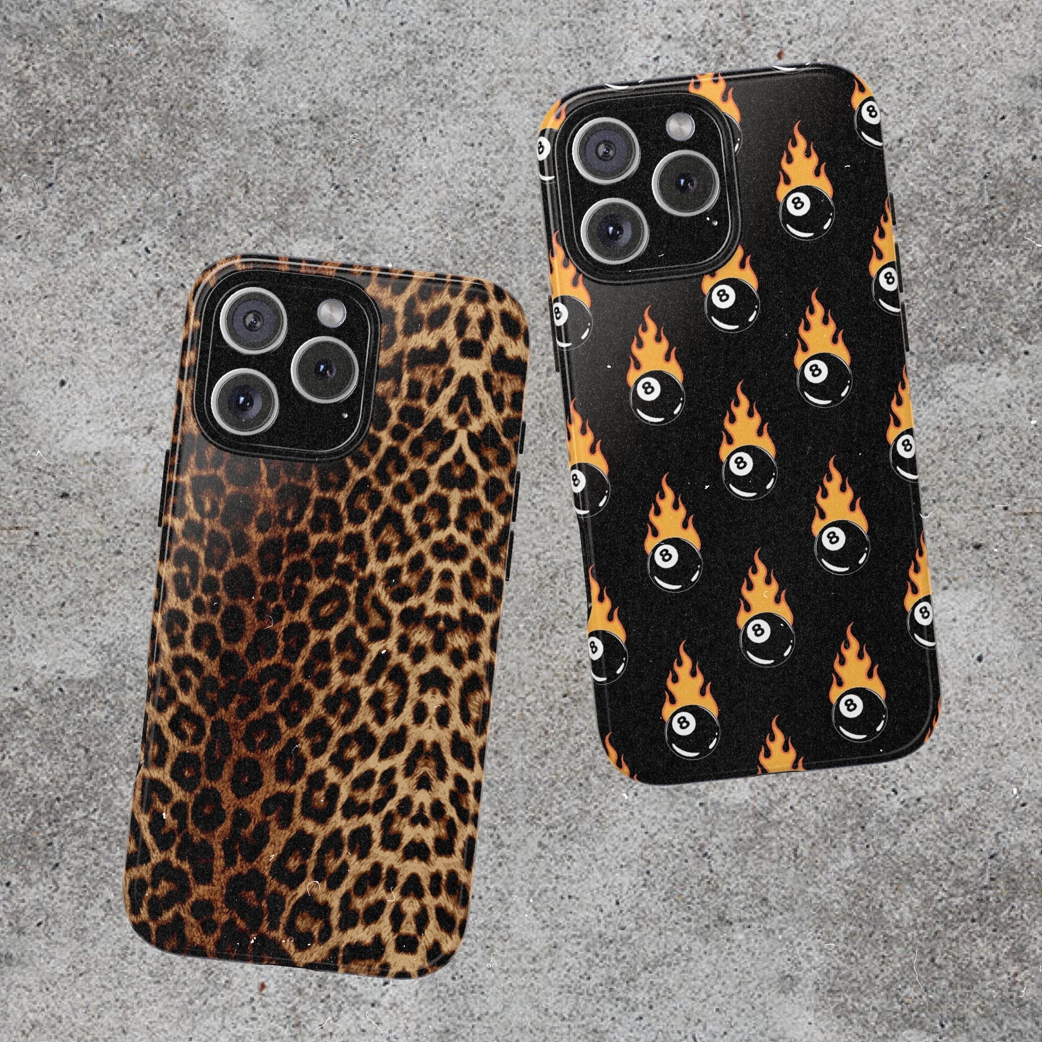 Two phone cases laid on concrete ground featuring leopard print and flaming 8 balls