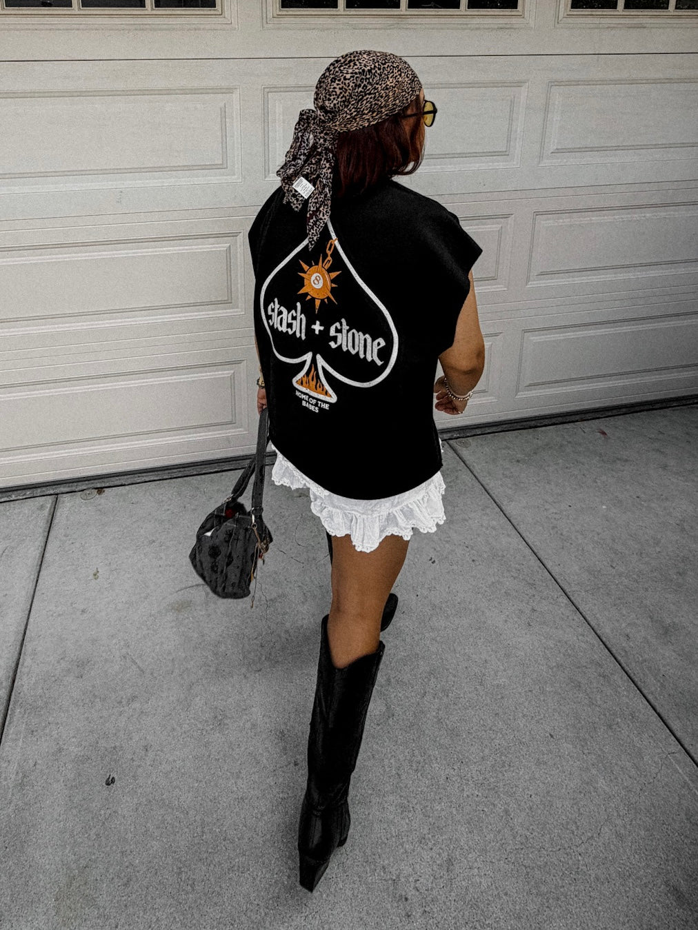 Person wearing a black sleeveless shirt with a design, white lace skirt, and black boots in front of a garage door.